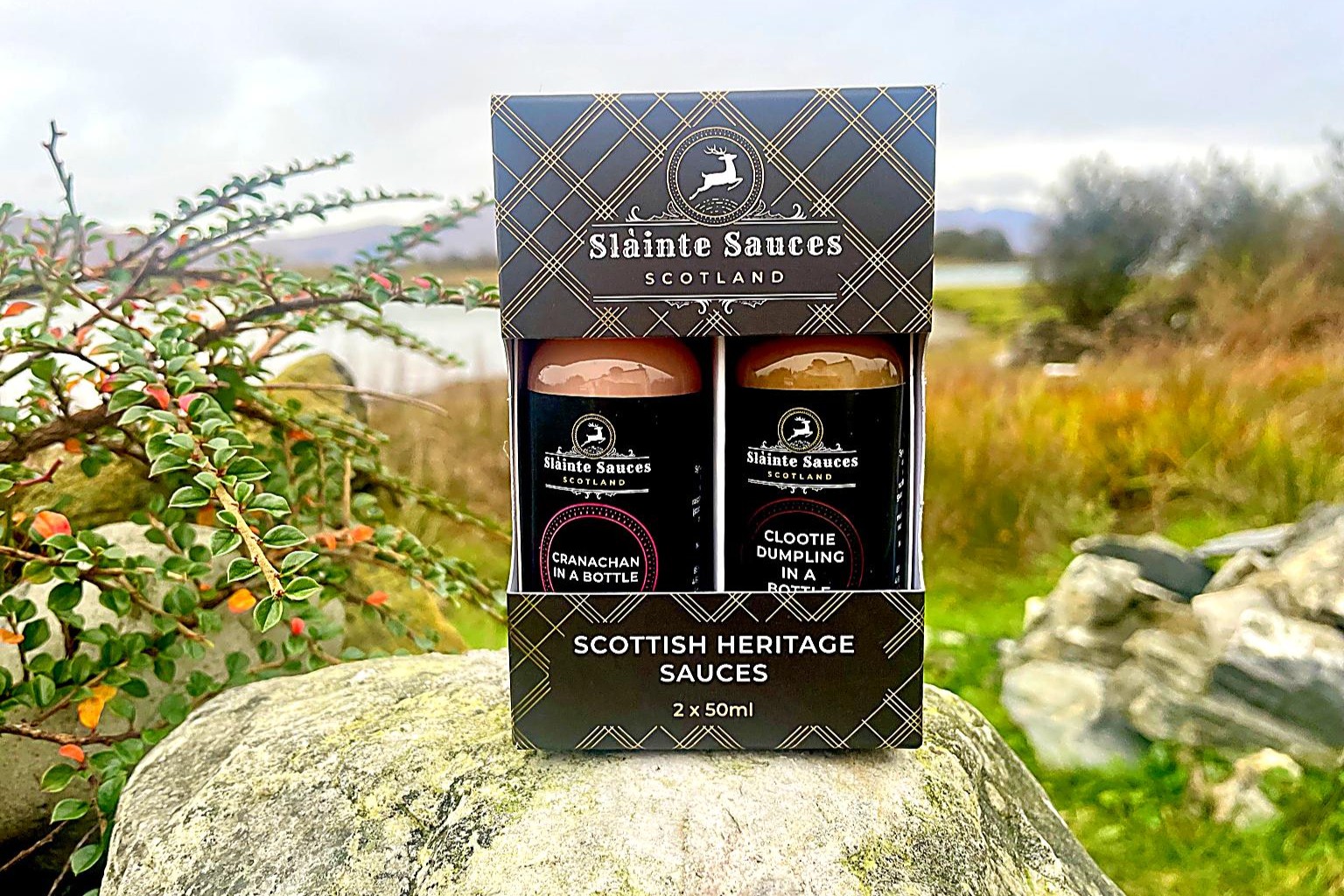 a two-bottle gift pack of Slàinte Sauces sitting on a rock with the banks of a scottish loch in the background